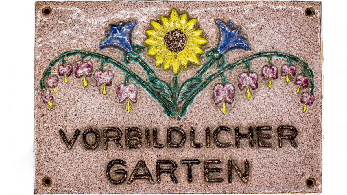 Foto: Schild mit einer Blumenranke, darunter die Aufschrift "Vorbildlicher Garten"