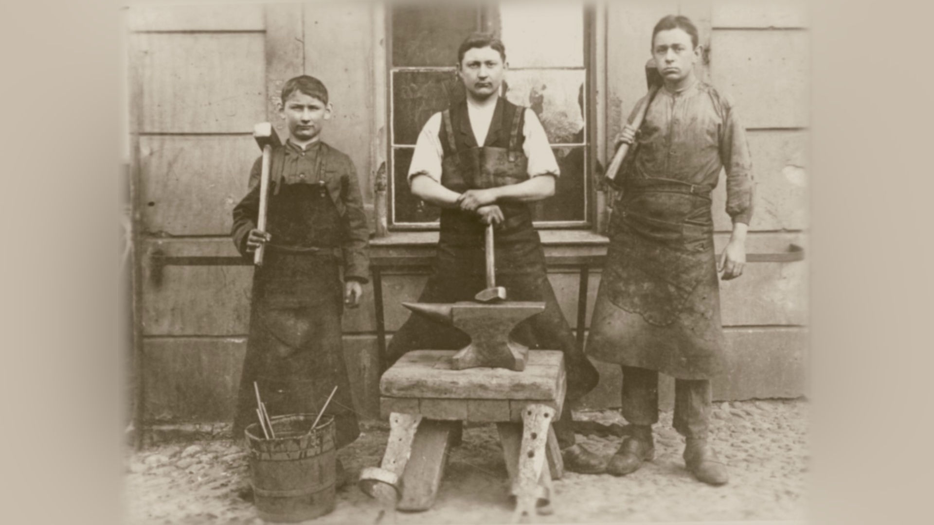 Foto: Drei Männer mit Hammern in der Hand, in der Mitte ein Amboss