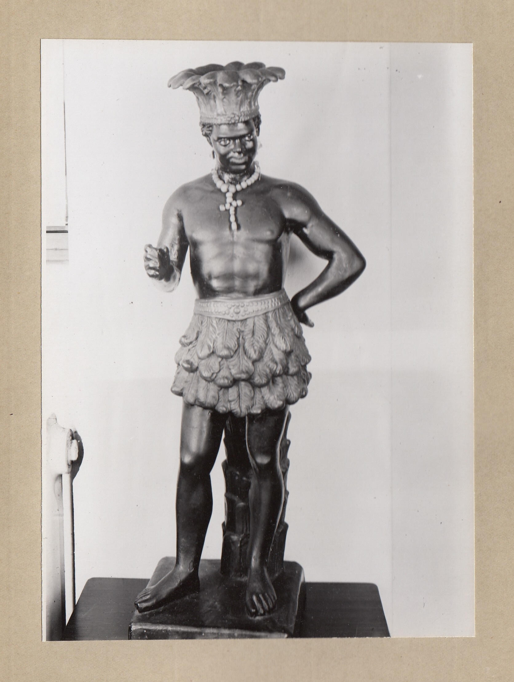 schwarz-weiß-Foto: dunkehäutige Schaufensterfigur mit gekleidet mit Federkrone und -schurz.